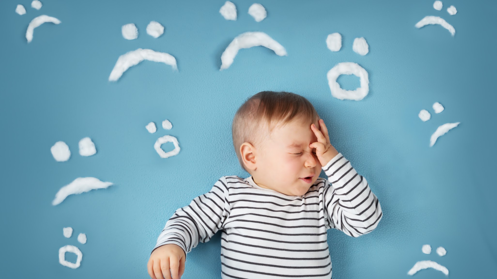 uhappy little boy on blue blanket background with sad smiley faces